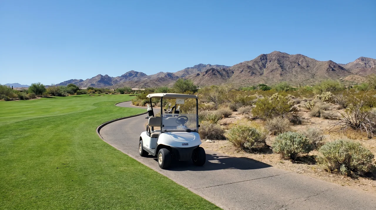 White golf cart parked on a paved cart path beside a desert golf course fairway