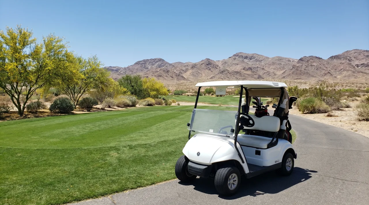 White golf cart on a path beside a fairway with Las Vegas desert landscape