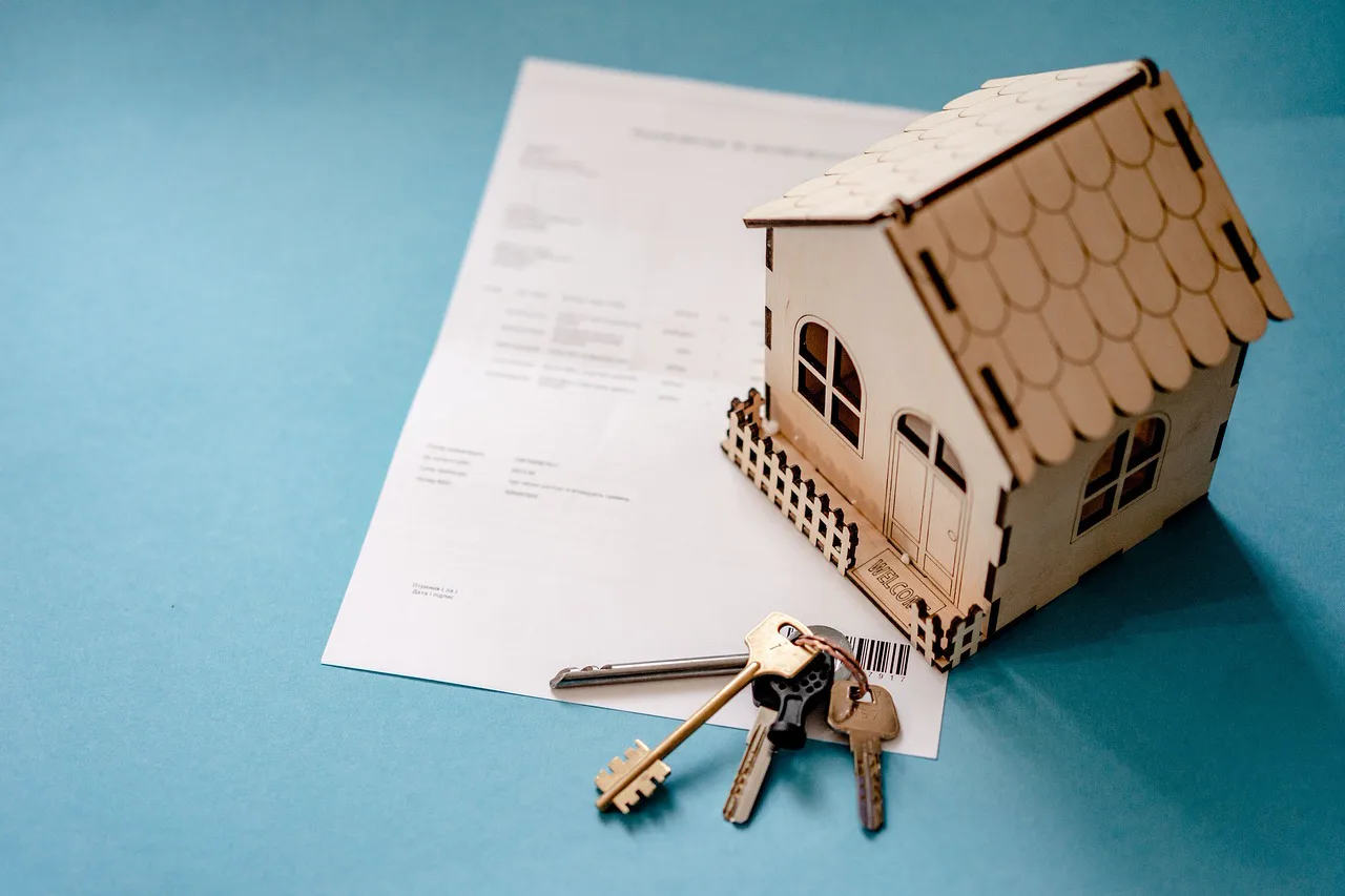 Hands holding house keys above rental property paperwork, a calculator, and a contract on a desk