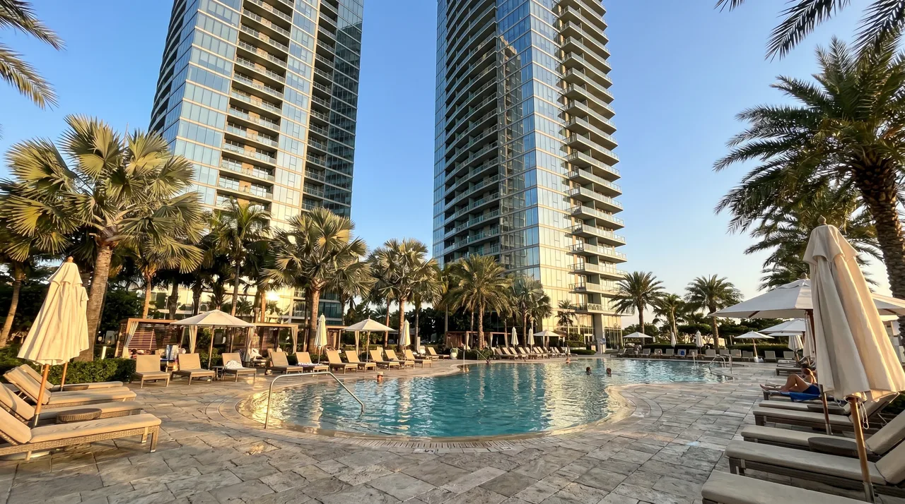 Luxury high-rise condominium towers rising above a resort pool deck with palm trees