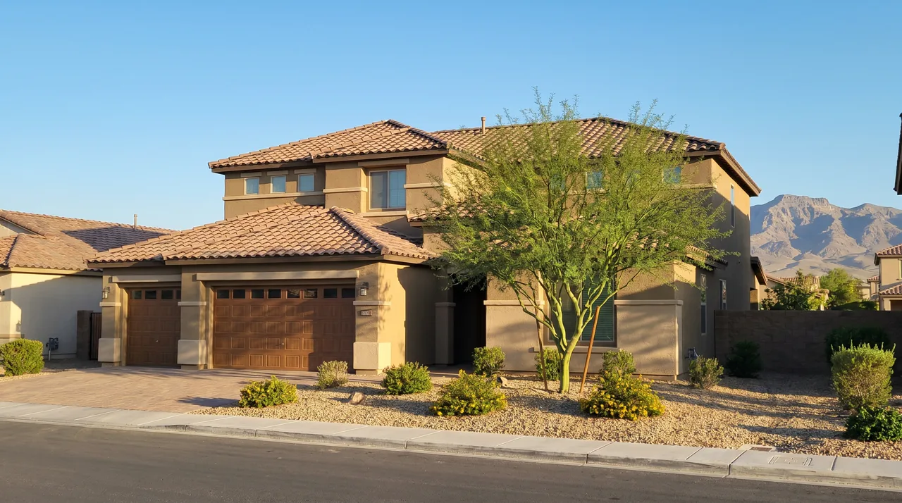 Modern two-story stucco single-family home with xeriscaped desert landscaping, three-car garage, and mountain views in the background