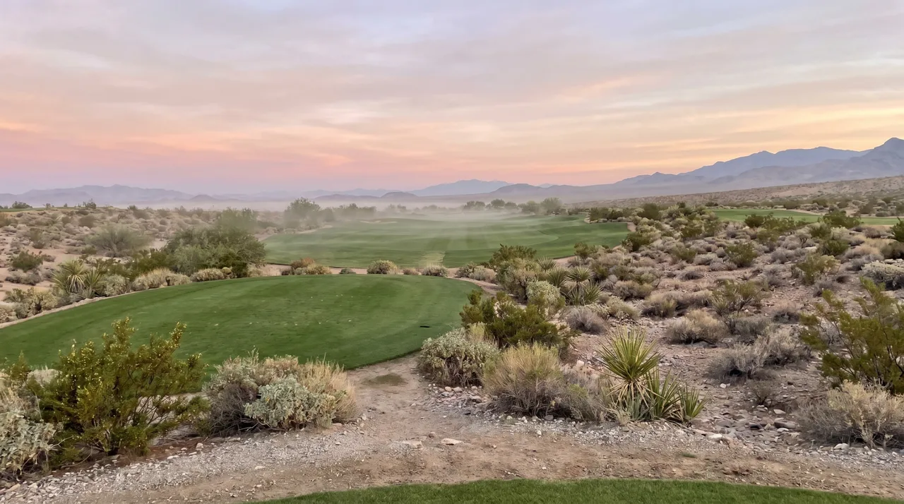 Wide view of an empty Las Vegas desert golf fairway at sunrise with mountains in the distance